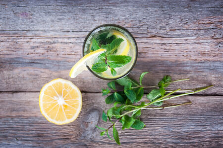 Lemonade with fresh lemon and mint in glass on wooden background