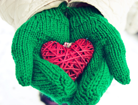 hands in green woolen mittens holding red heartの写真素材