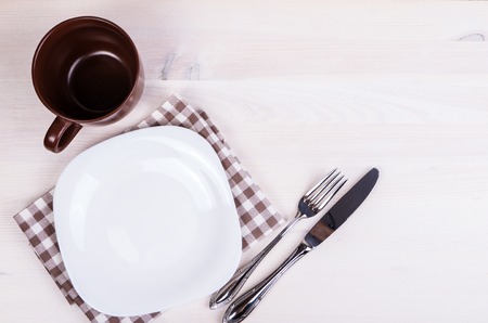 Fork with knife, blank plates, empty cup and napkin. On wooden table backgroundの写真素材