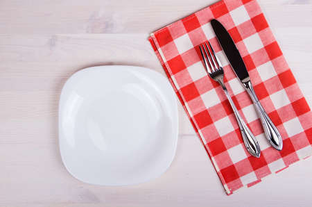 Empty dish, knife and fork and red napkin on wood tableの写真素材