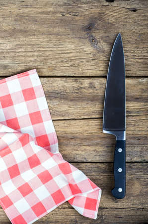Cutting breadboard and knife over red grunge gingham tablecloth backgroundの写真素材