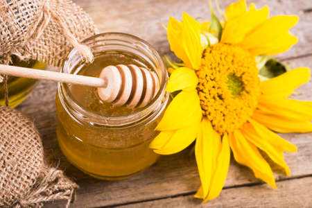 A jar of honey with sunflowers and spoon on old wooden backgrounの写真素材