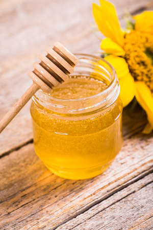 A jar of honey with sunflowers and spoon on old wooden backgrounの写真素材