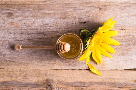 A jar of honey with sunflowers and spoon on old wooden backgrounの写真素材