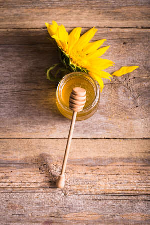 A jar of honey with sunflowers and spoon on old wooden backgrounの写真素材