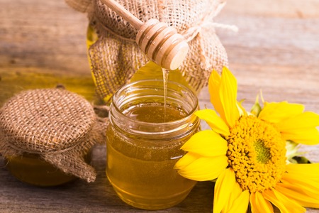 A jar of honey with sunflowers and spoon on old wooden backgrounの写真素材