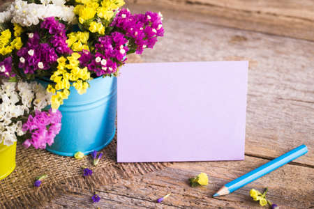 Dried flowers in brightly colored buckets with a pencil and a card on a wooden backgroundの写真素材