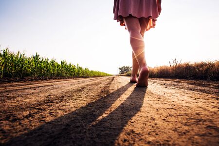 woman goes barefoot at sunset on field roadの写真素材