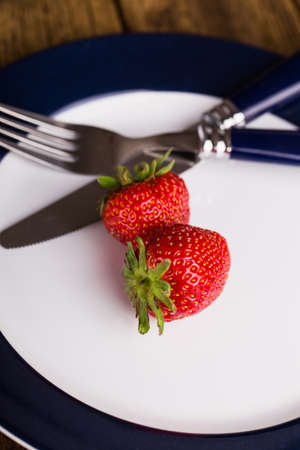 strawberries on a plate with knife and fork on wooden backgroundの写真素材