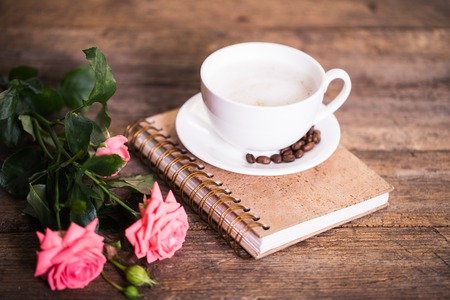 cup of coffee with milk and pink roses and books on the old wooden backgroundの写真素材