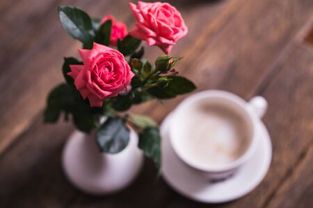 cup of coffee with milk and pink roses on old wooden backgroundの写真素材