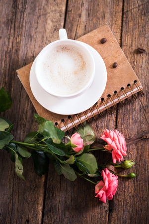 cup of coffee with milk and pink roses and books on the old wooden backgroundの写真素材