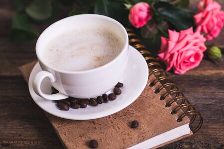 cup of coffee with milk and pink roses and books on the old wooden backgroundの写真素材