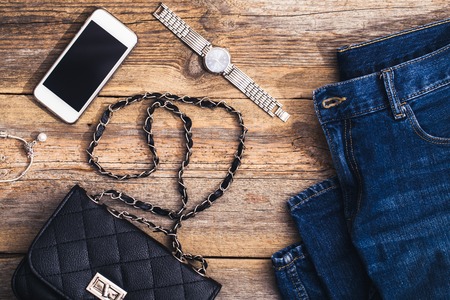 Fashion accessories for a young girl, watch, bracelet, handbag, red lipstick, telephone, brush on a wooden background.の写真素材