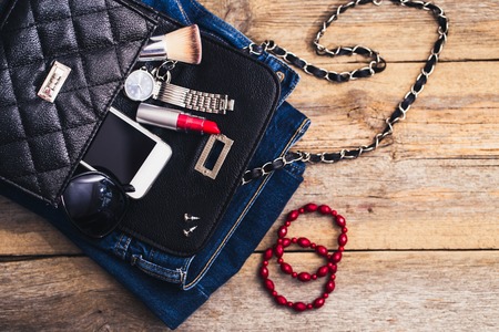 Fashion accessories for a young girl, watch, bracelet, handbag, red lipstick, telephone, brush on a wooden background.の写真素材