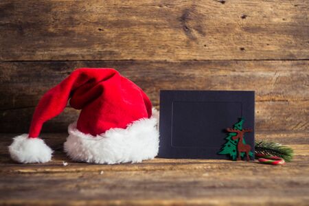 Christmas cards and gifts with Santa hats on wooden background with candy cane, fir branches, candle, cones.の写真素材