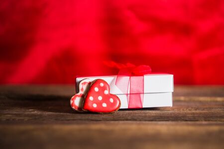 White gift box with red hearts and ribbon on a wooden background.