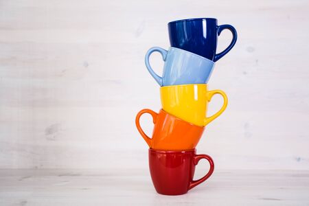 a stack of colorful coffee cups on a white wooden background