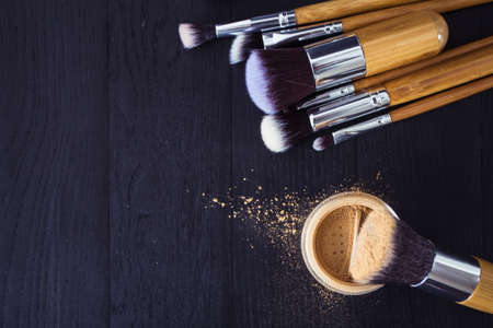 make up brushes with powder and rouge on a black wooden background
