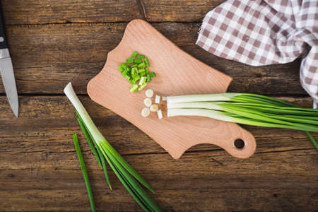 Green onions on a chopping board. Knife and napkin on a wooden tableの写真素材