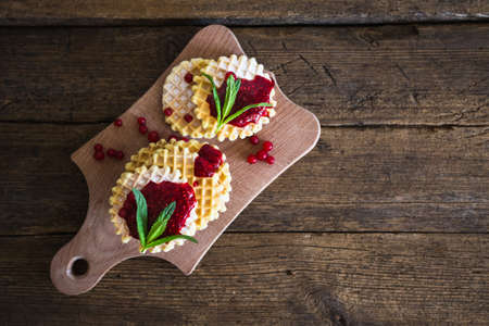 Waffle with berry jam, powdered sugar and mint on black background