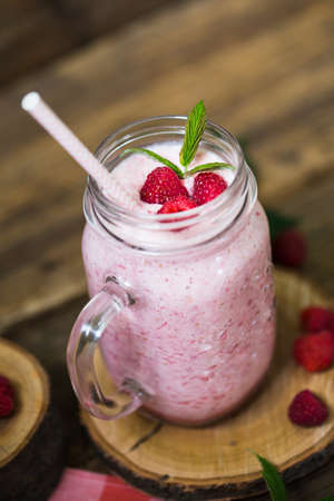 Pink raspberry smoothie in a mason jar with straws on a rustic wood backgroundの写真素材