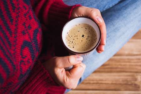 young woman in a red sweater holding a cup of coffeeの写真素材