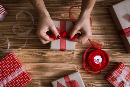 Female hands wrapping xmas gifts into paper and tying them up with red and white threadsの写真素材