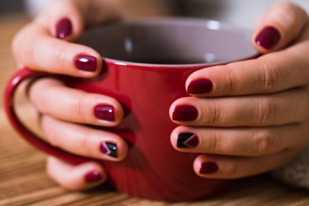 Woman with red manicure holding a red cup of teaの写真素材