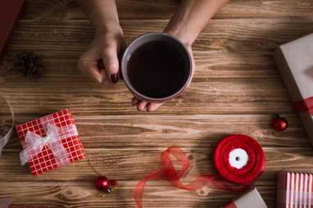 Female hands wrapping Christmas presents in paper and tying them with red and white threads and a cup of teaの写真素材
