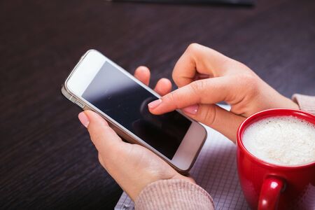 A woman holding a smart phone and a red cup of coffee. gift box with red ribbon and white notebookの写真素材