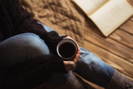 Woman with beautiful manicure holding a gray cup of tea and reading a bookの写真素材