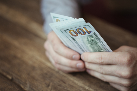 Male hands holding dollar banknote on old wooden backgroundの写真素材