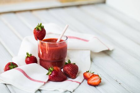 A glass of strawberry smoothie on a white wooden backgroundの写真素材