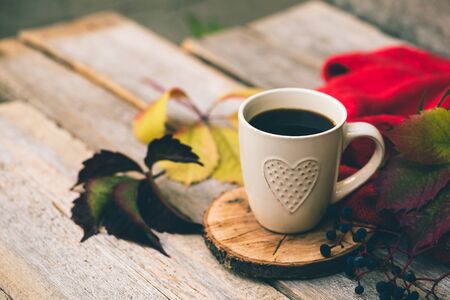 Mug of hot coffee in autumn setting on a wooden table with a knitted scarf, sweater.の写真素材
