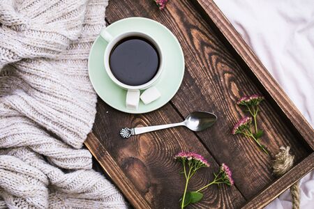 Cup of coffee and candle on rustic wooden serving tray and knitting warm woolen sweater