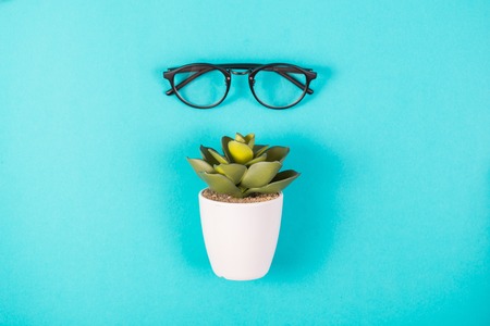 Glasses and artificial plant in a white pot on a blue backgroundの写真素材