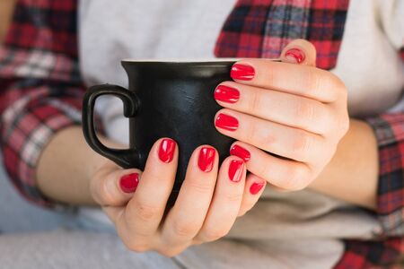 Beautiful young woman drinking coffee cappuccino, perfect red gel lacquer manicure.の写真素材