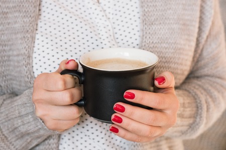Beautiful young woman drinking coffee cappuccino, perfect red gel lacquer manicure.