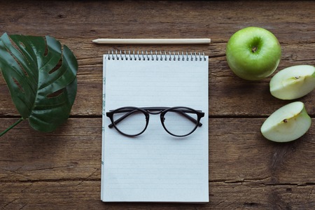 Top view of green apple, notepad and pencil on wooden background