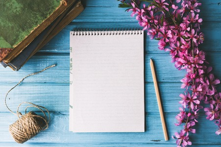 Blank notebook and wild flowers on blue wooden background. Concept flowers of spring,