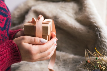 A woman holding a Christmas gift with a ribbon on a wooden table. Christmas presents and New Yearの写真素材