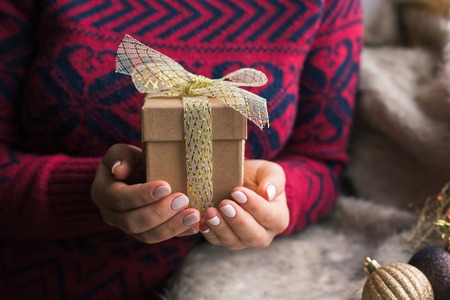 A woman holding a Christmas gift with a ribbon on a wooden table. Christmas presents and New Yearの写真素材