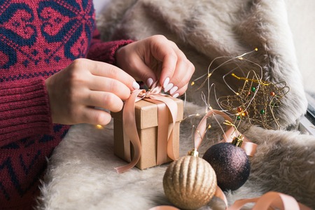 A woman holding a Christmas gift with a ribbon on a wooden table. Christmas presents and New Year