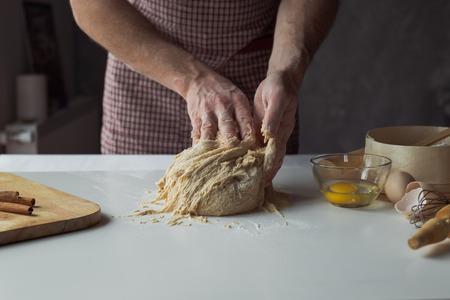 A handful of flour with egg on a rustic kitchen. Against the background of men's hands knead the...