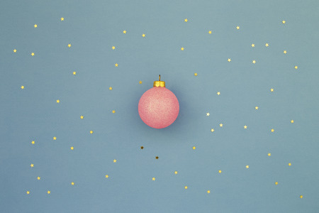 Pink Christmas ball on blue holiday background with gold stars sequins. Minimal New Year greeting card. Shining Night sky at christmas conceptの写真素材