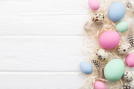 Easter eggs, straw and feathers on white rustic wooden table. Top view, copyspace. Holiday Frame in pastel colorsの写真素材