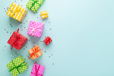 Holiday flat lay with gift boxes wrapped in colorful paper and tied with bows on blue background, decorated with confetti. Birthday, Christmas and sale concept, top view.の写真素材