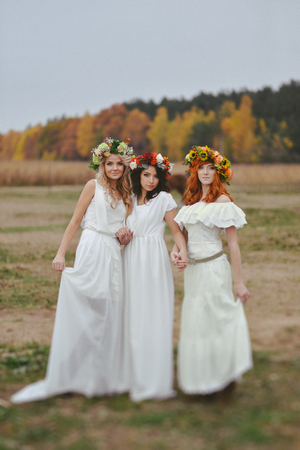 three colors of autumn. three girls in autumn wreaths stand on natureの写真素材