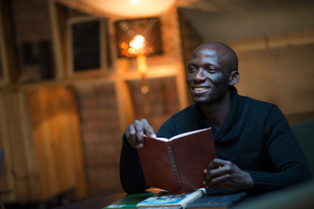 A young Arican man is reading a book in a room at a table. student, businessmanの写真素材